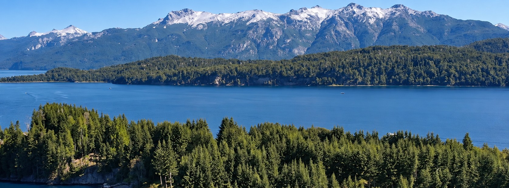 Aerial view of the snow-capped Andes mountain range rising above a lake and Southern Chile's forested foothills